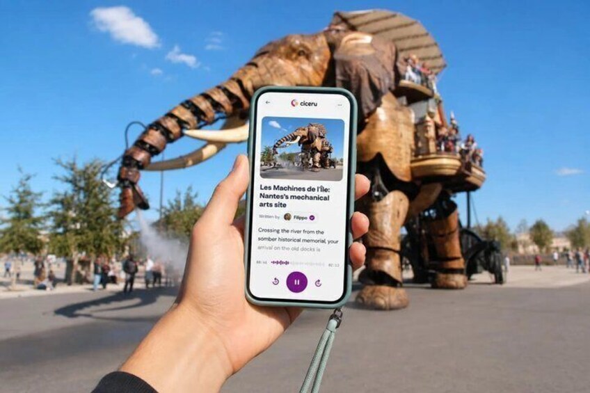A hand holding a smartphone displaying a photo of a mechanical elephant sculpture. 1