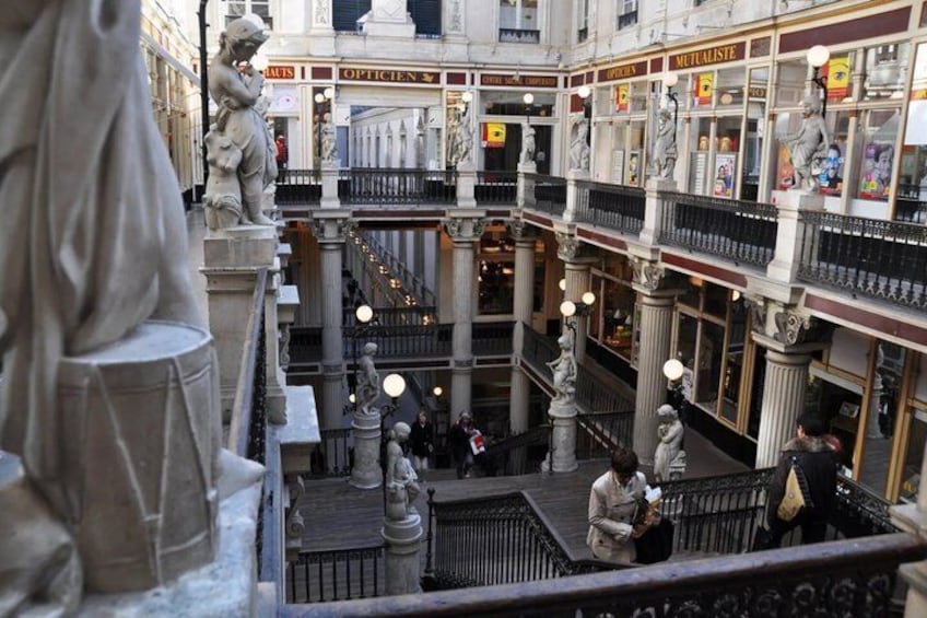 A multi-level shopping arcade with statues, columns, and various shops. 3