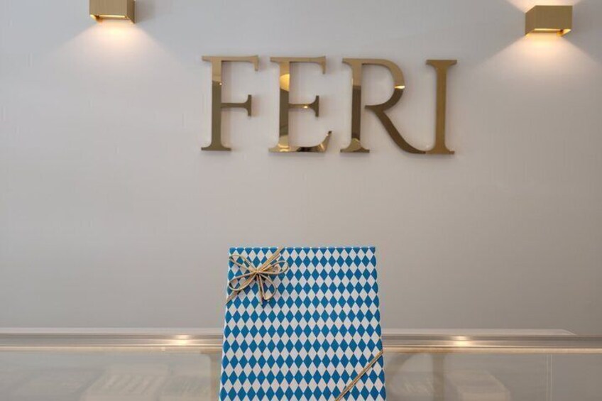 A wall with the word 'FERI' in gold letters, a patterned gift box, and two wall-mounted lights. 3