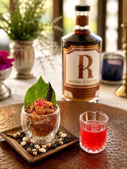 Et glas rød drik, en flaske Hong Kong Rum og en skål mad med en bladpynt på et struktureret bord. 5