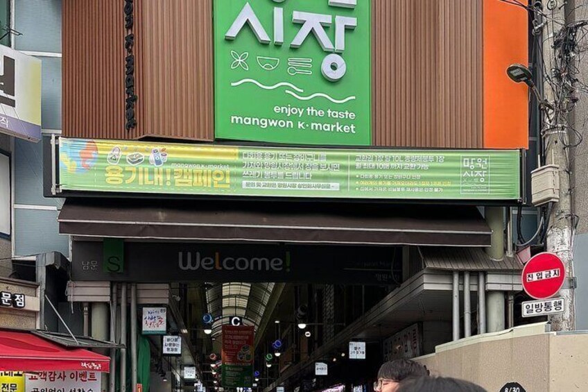 A market entrance with a green sign, a welcome sign, and various directional signs. 4
