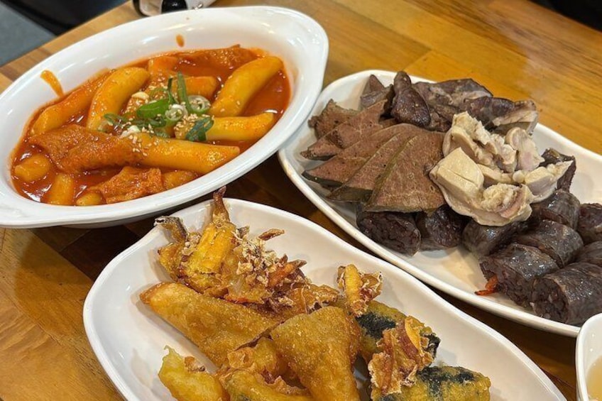A table with three dishes: a bowl of red sauce with noodles, a plate of sliced meat, and fried fish. 1
