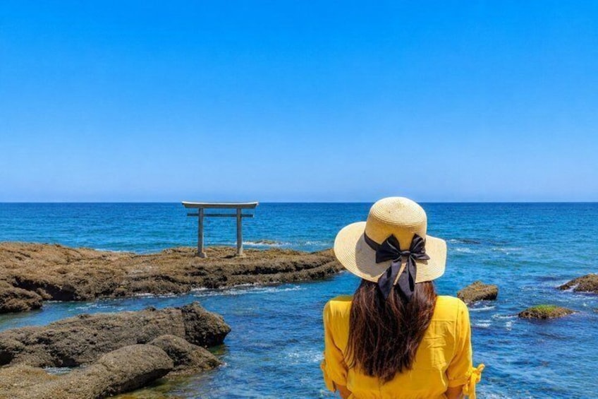 A person in a yellow shirt and straw hat, facing a rocky shoreline with a wooden structure. 1