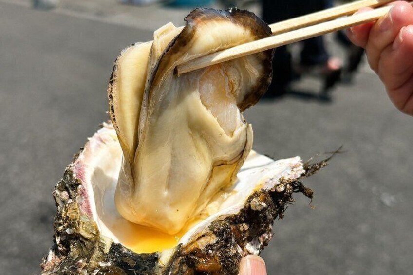 A person holding a half-open oyster with a pair of chopsticks. 2