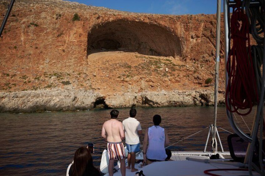 A group of people on a boat near a rocky coastline with a cave-like formation. 3