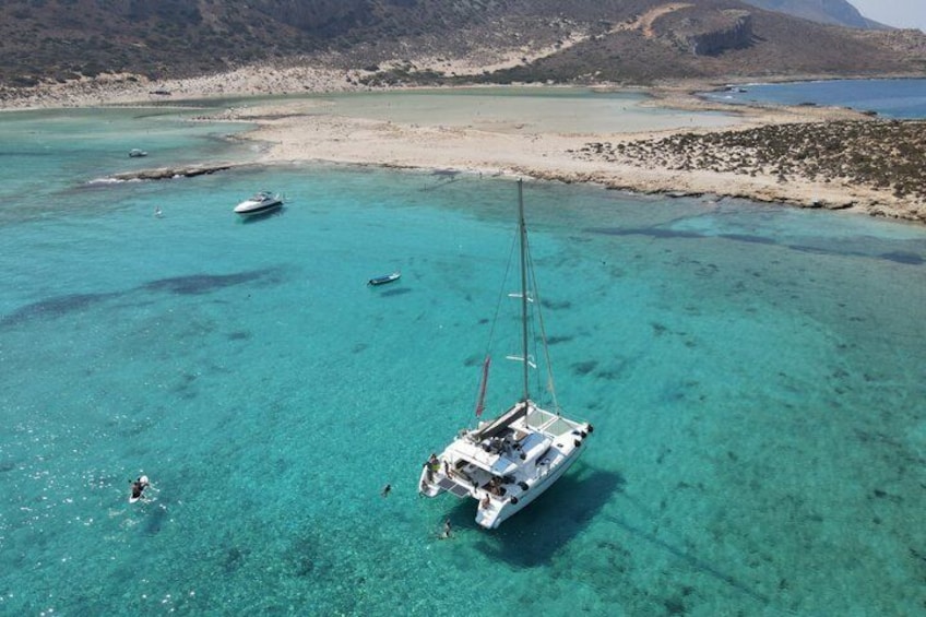 A sailboat anchored in clear turquoise waters with a sandy beach and rocky hills in the background. 2