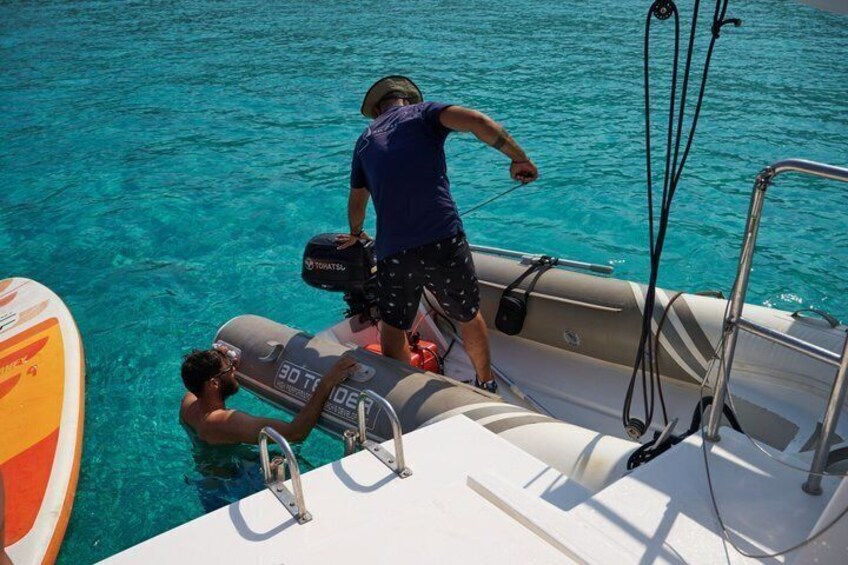 A person on a boat, another person on a float, and a surfboard in the water. 5