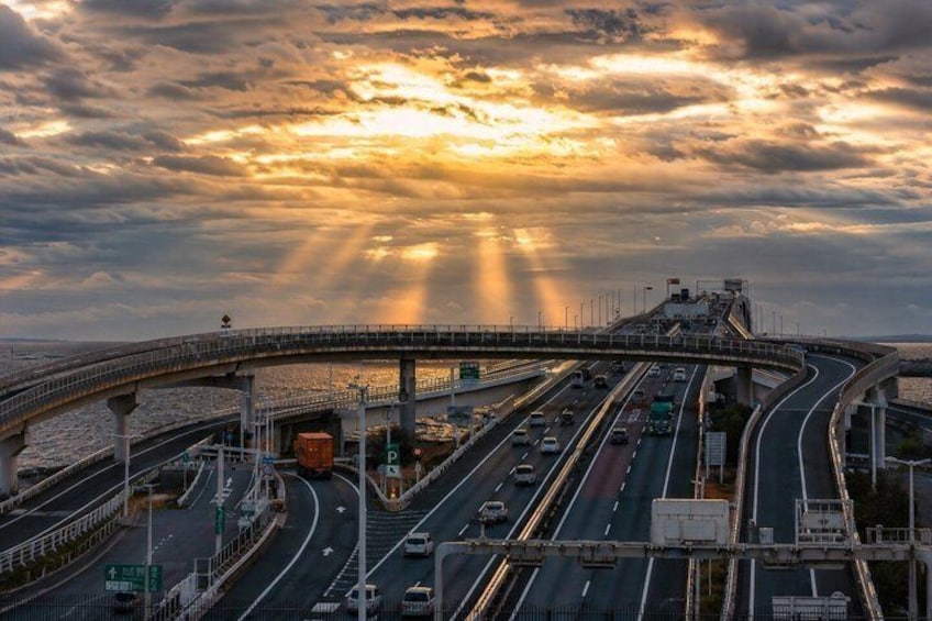 A multi-level highway interchange with vehicles, a bridge, and a sunset. 3