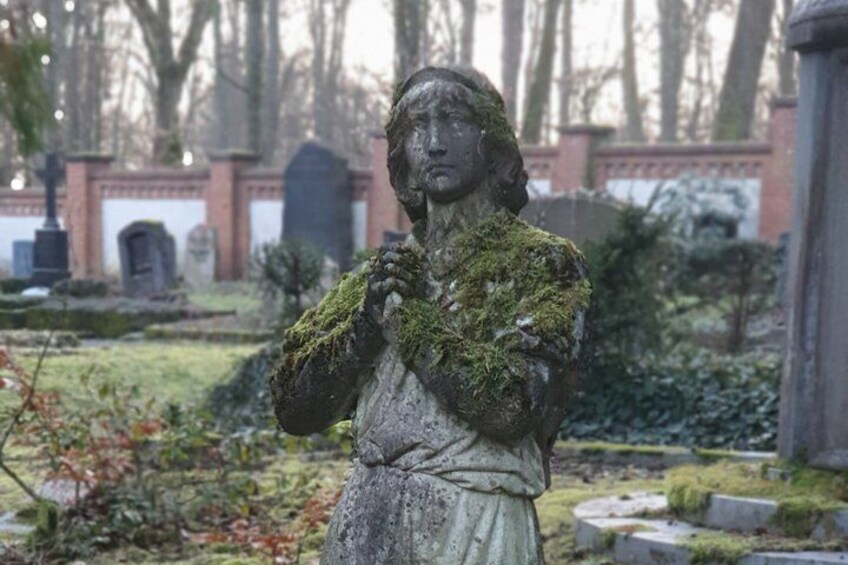 A statue of a woman with moss, surrounded by gravestones in a cemetery. 2