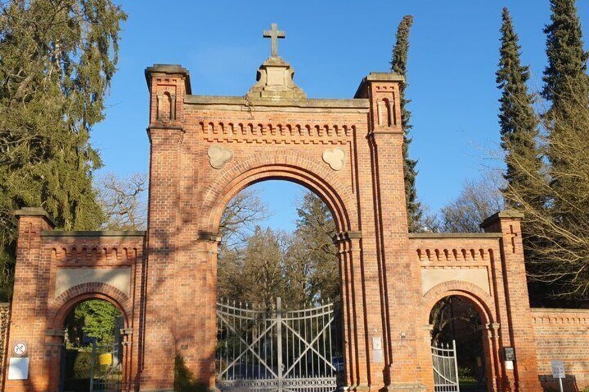 A brick archway with a cross on top, surrounded by trees. 1
