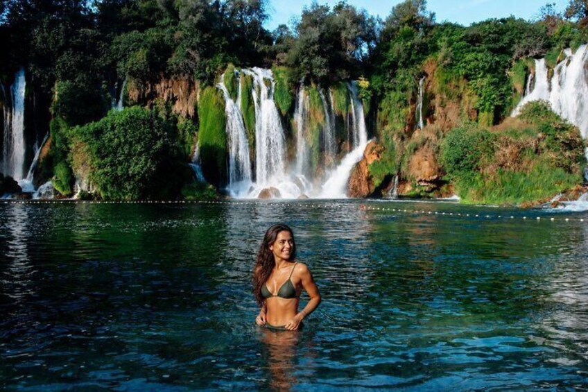 A woman in a bikini standing in a body of water with multiple waterfalls in the background. 2