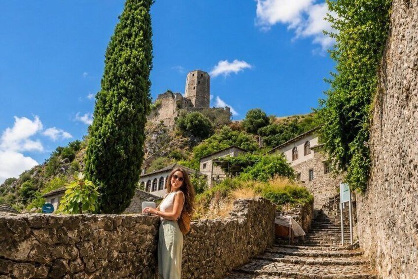A woman standing on a stone wall overlooking a village with a castle on a hill. 3