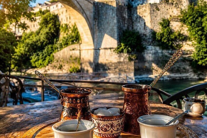 A table with traditional Turkish coffee cups and a metal pot, set against a backdrop of a stone bridge and greenery. 5