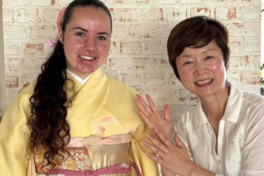 Two people, one in traditional attire and the other in a white shirt, standing in front of a brick wall. 1