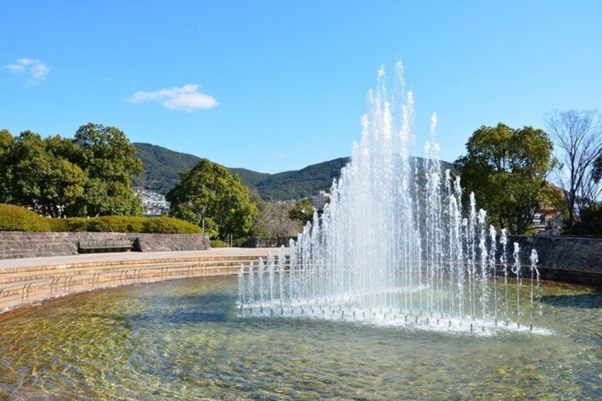 A fountain with water jets, a stone wall, and trees in the background. 4