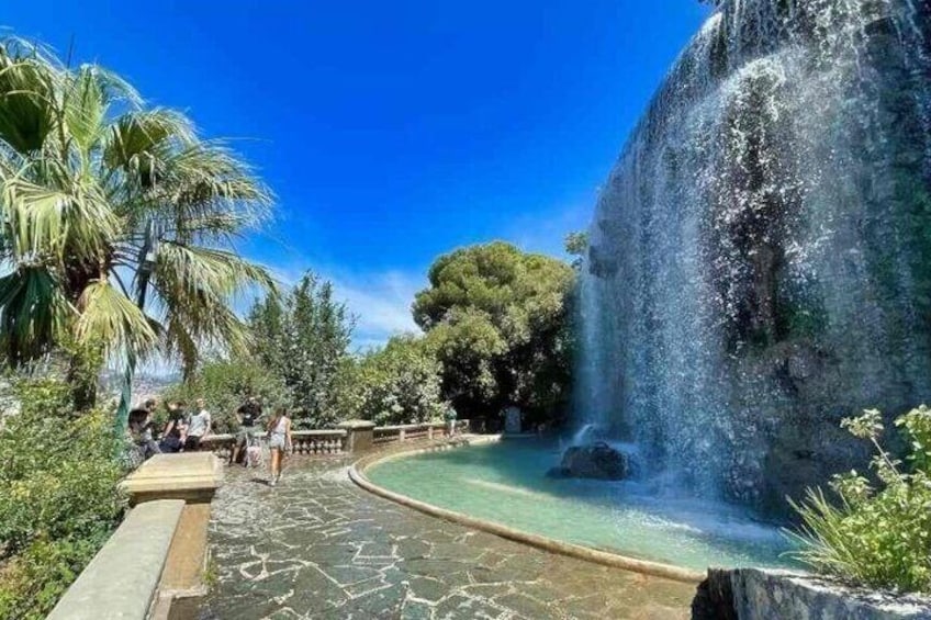 A waterfall, a pool, and a pathway with palm trees and greenery. 5