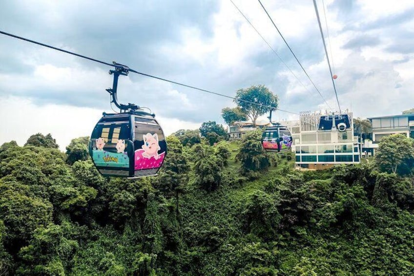 A cable car system with passengers, surrounded by dense greenery and a modern building. 4
