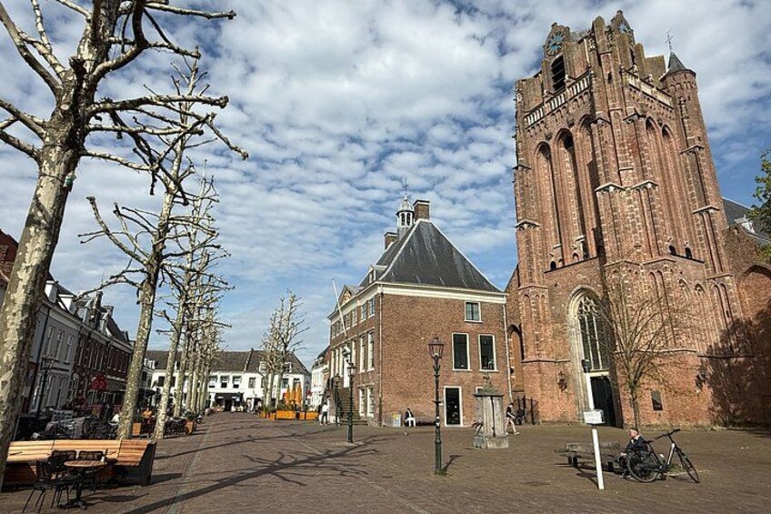 A historic building with a tall tower, a paved square, and leafless trees. 4