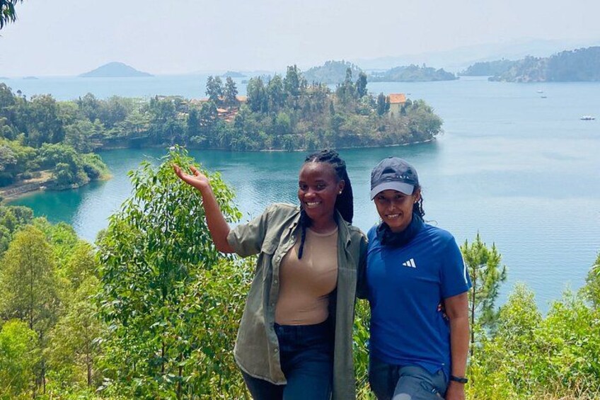 Two people standing on a hill overlooking a lake with trees and a distant island. 1