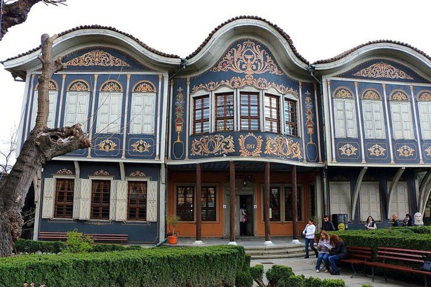 A building with ornate blue and gold detailing, large windows, and a bench in the foreground. 3