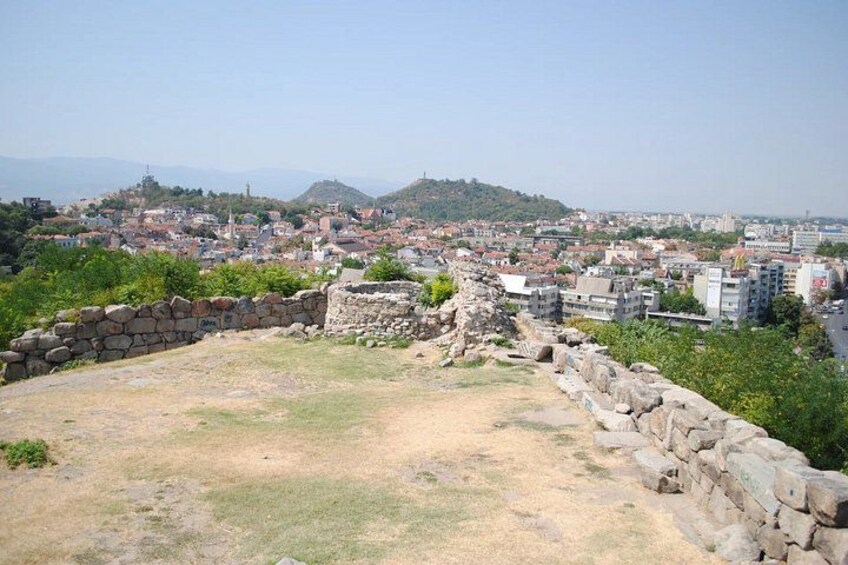 A historical site with ancient ruins and a view of a modern cityscape in the background. 2