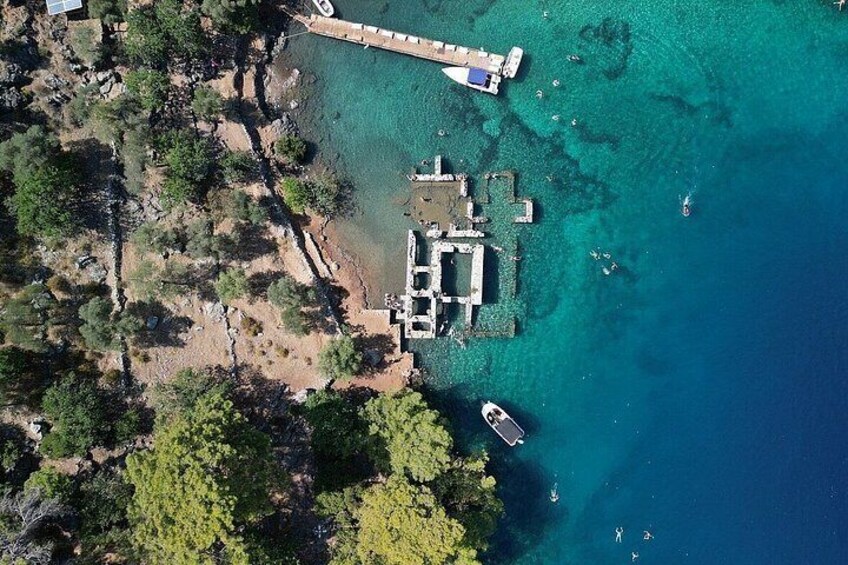 An aerial view of a coastal area with a pier extending into turquoise waters, surrounded by dense greenery and rocky terrain. 4