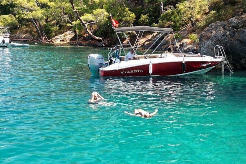 A boat named 'V. LESTA' on clear turquoise water, a swimmer in the water, and a rocky shoreline with trees. 5