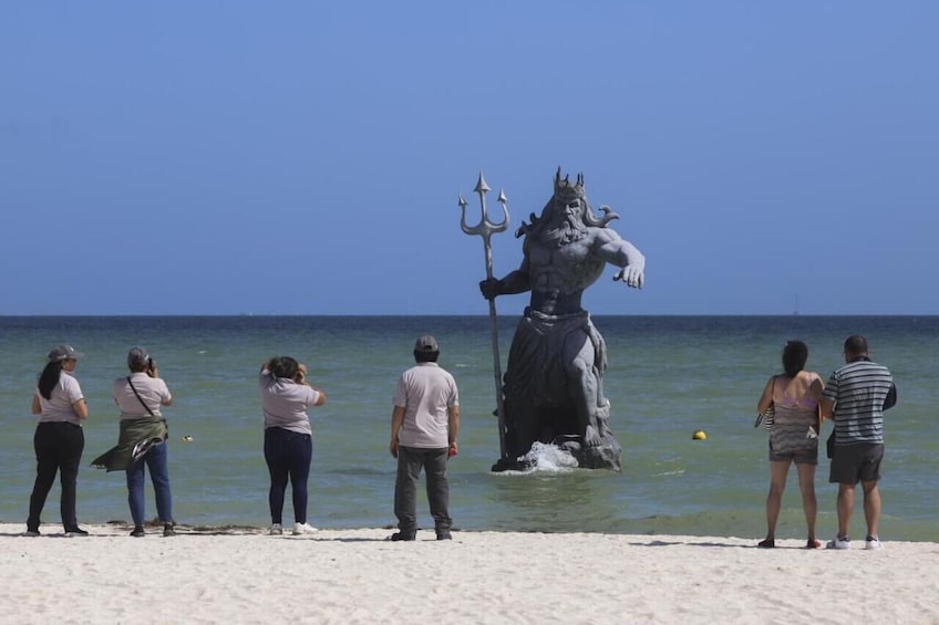 A statue of a mythological figure on a beach with people observing it. 2