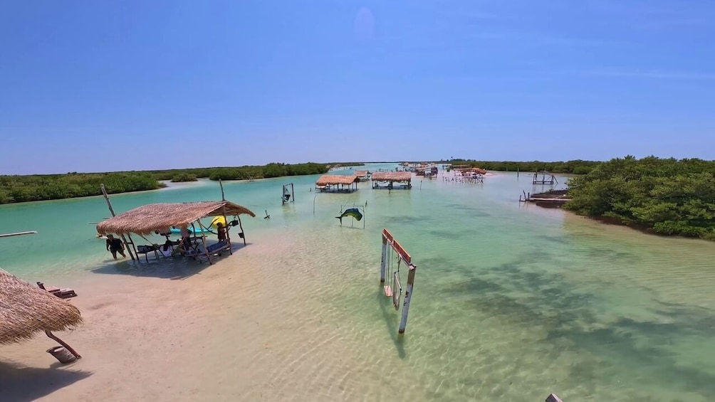 A beach with clear turquoise water, a thatched-roof hut, and a pier extending into the sea. 1