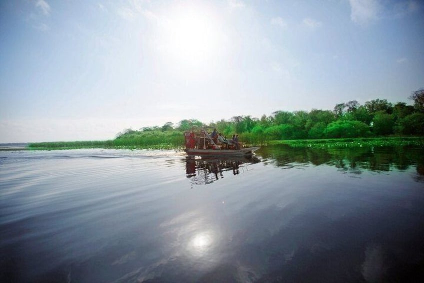 A calm river with a boat carrying passengers, surrounded by lush greenery. 5