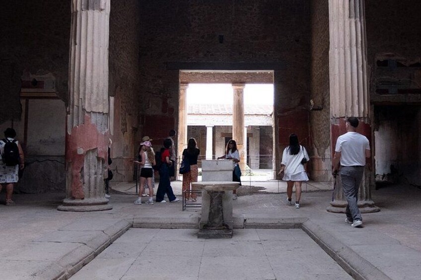 An ancient building with columns, a central fountain, and visitors. 4