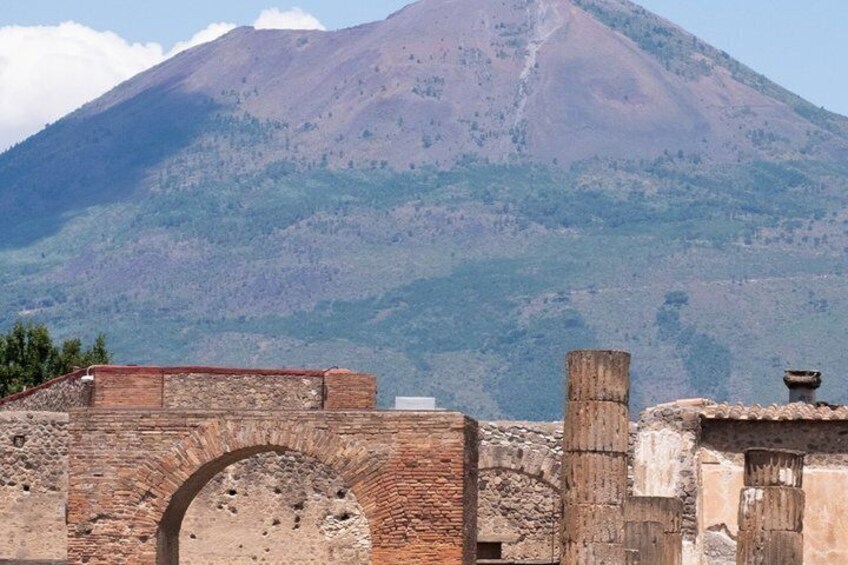 A mountain with a volcano, ancient brick ruins, and a wooden structure. 1
