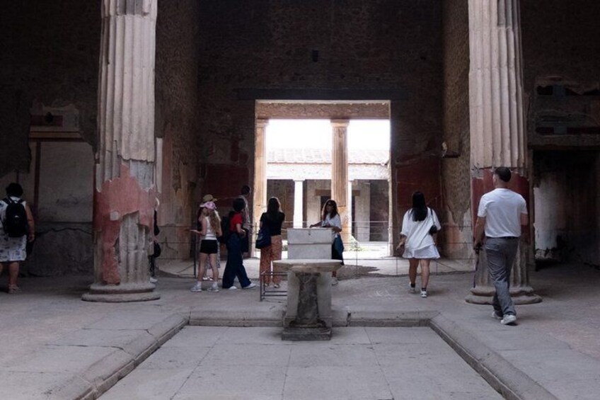An ancient building with columns and a central fountain. People are walking around. 4