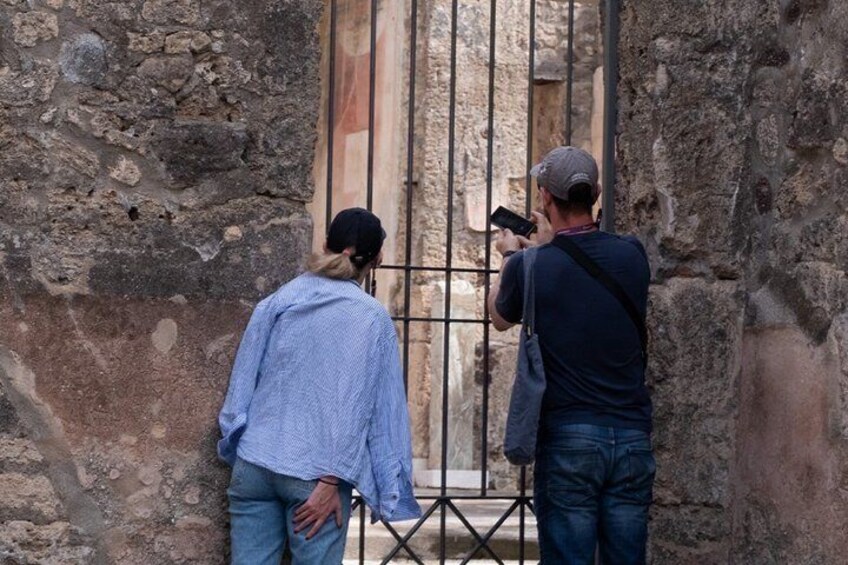 Two people taking a photo of an old stone building with a barred window. 2