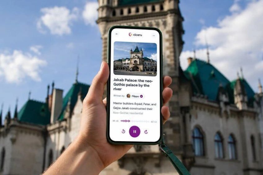 A hand holding a smartphone displaying a photo of a historic building with a neo-Gothic palace by the river. 1