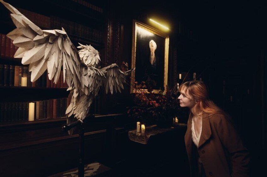 A person in a library with bookshelves, a large winged sculpture, and a framed picture on the wall. 5