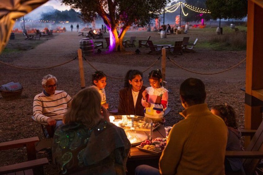 A group of people dining outdoors at night with string lights and a tree in the background. 4