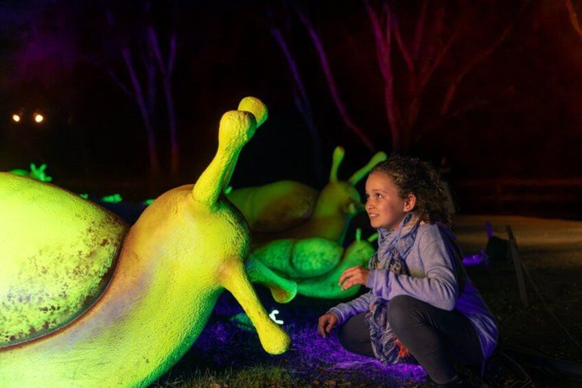A person crouching next to a large illuminated sculpture of a snail. 2