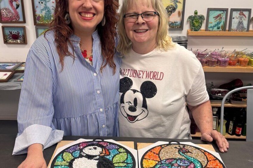 Two people standing behind a table with colorful artwork. 2