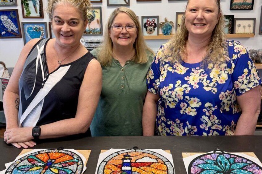 Three people standing behind a table with mosaic artwork. 1