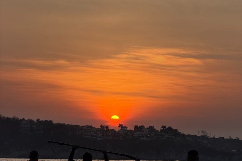 A sunset over a coastal area with silhouettes of people and a boat. 1