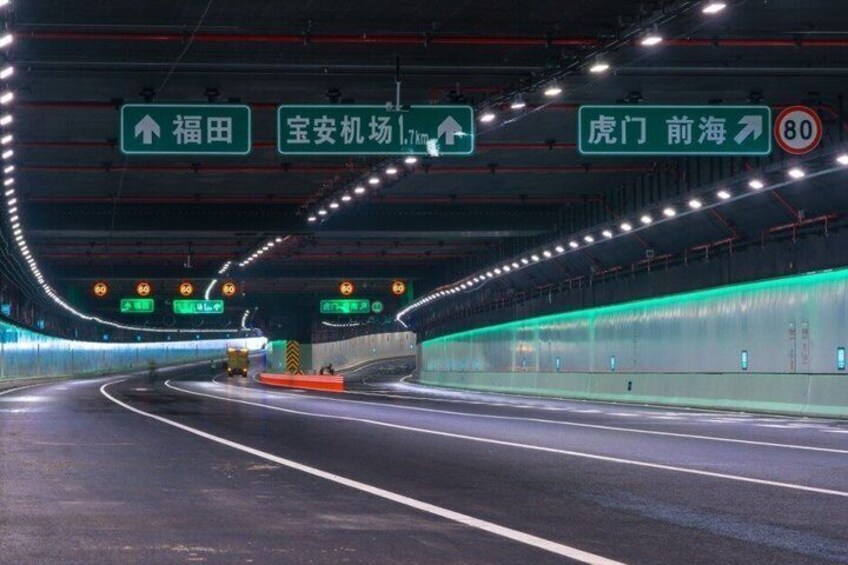 A multi-lane highway with overhead directional signs, a speed limit sign, and a tunnel entrance. 3