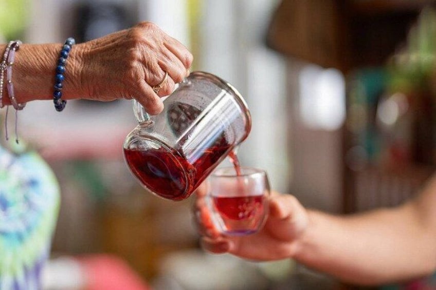 A person pouring a red liquid from a clear glass jug into a glass. 4
