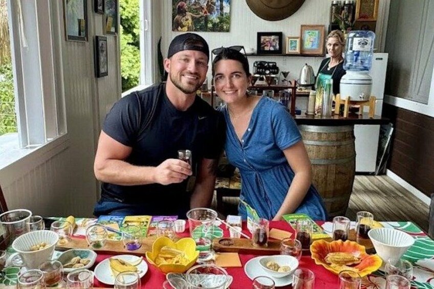 A dining table with various dishes and drinks, a kitchen in the background, and a person wearing a black shirt. 3