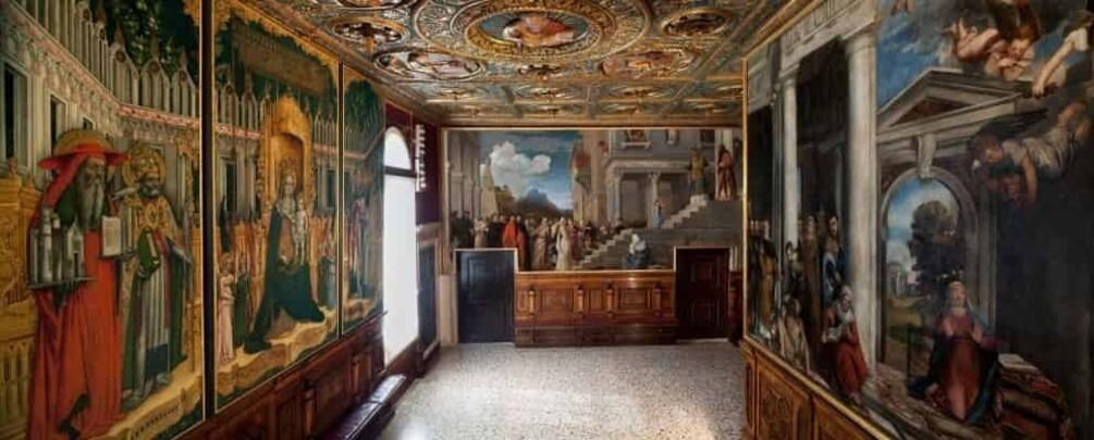 An ornate hallway with frescoes and a large painting on the walls. 1