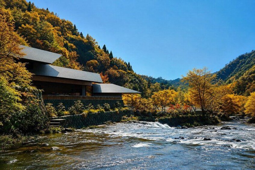 A modern building with a sloped roof, surrounded by autumn-colored trees and a flowing river. 4