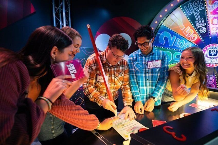 A group of people at a gaming booth with a wheel and cards. 3