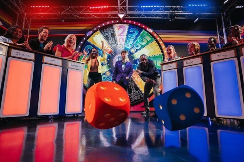 A game show set with a spinning wheel, a large red die, and a blue die. 1