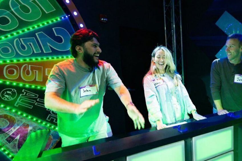 A stage with a DJ booth, a neon sign, and a person holding a microphone. 4