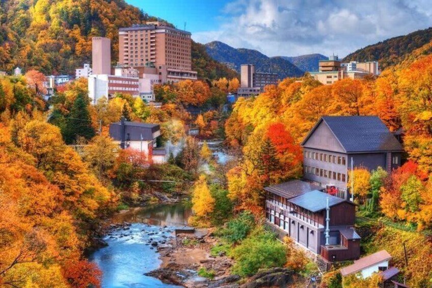 A river flowing through a town surrounded by autumn-colored trees, with buildings and a mountain in the background. 2